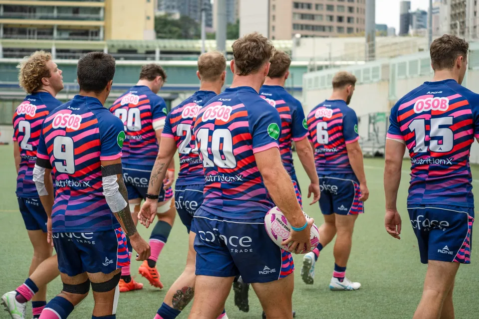 OSOB players walk onto the pitch in navy and pink striped shirts