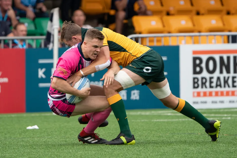 OSOB ball carrier is hit head-on by a Classic Wallabies tackler in green and gold as teammates in pink support