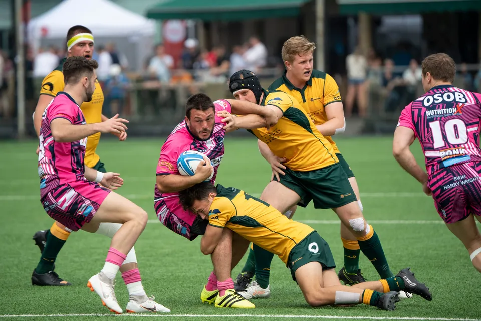 OSOB ball carrier in pink is dragged down low by a Wallabies tackler as number 10 runs in from the right