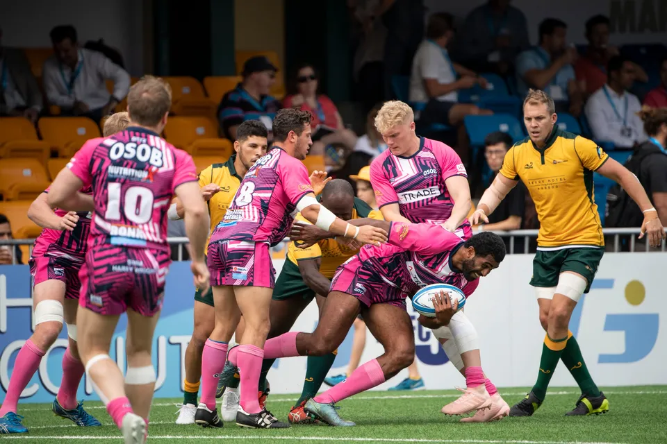 OSOB players in pink gather around their ball carrier in a contact, a Wallabies defender in green and gold nearby