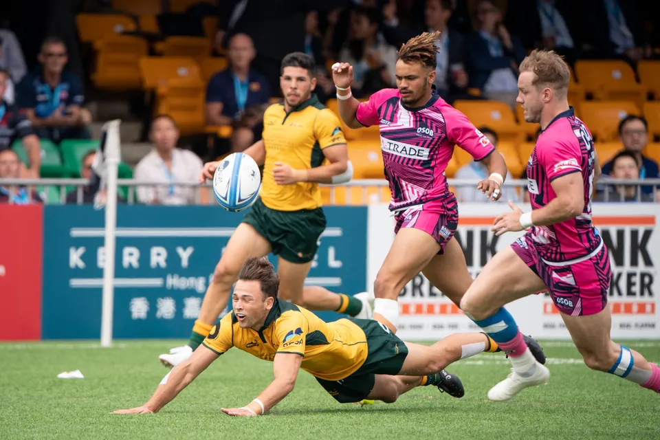 Wallabies runner holds the ball upright as a teammate dives beside him and OSOB players in pink chase