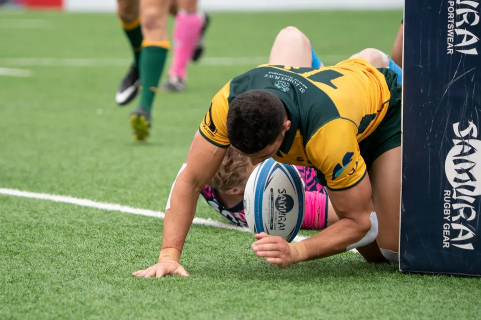 Classic Wallabies player dives to put the ball down by a padded post near the try line, an OSOB player beneath him
