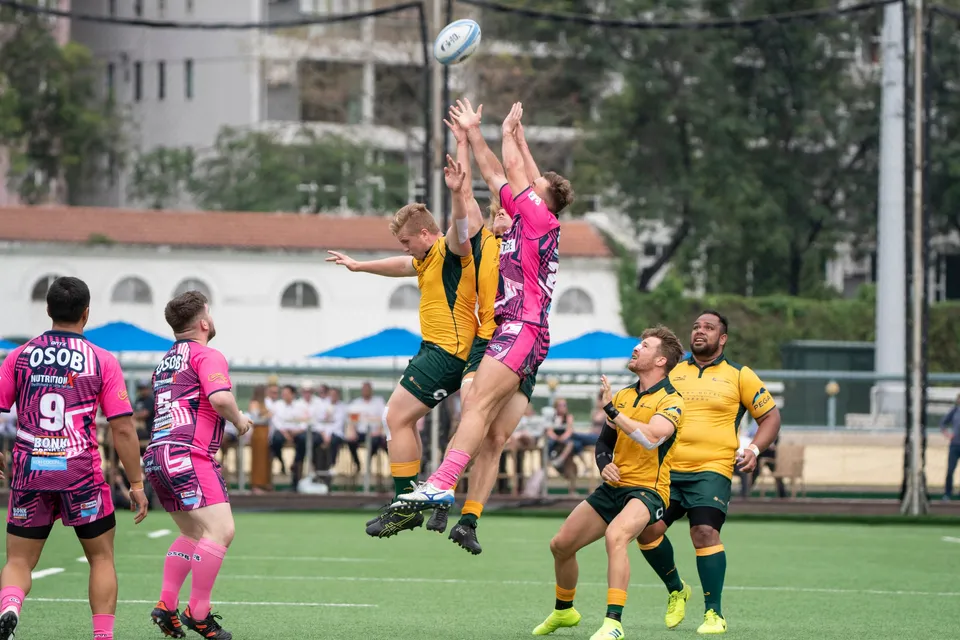 OSOB jumper and a Classic Wallabies jumper leap together for the ball in a line-out, pink-shirted players to the left