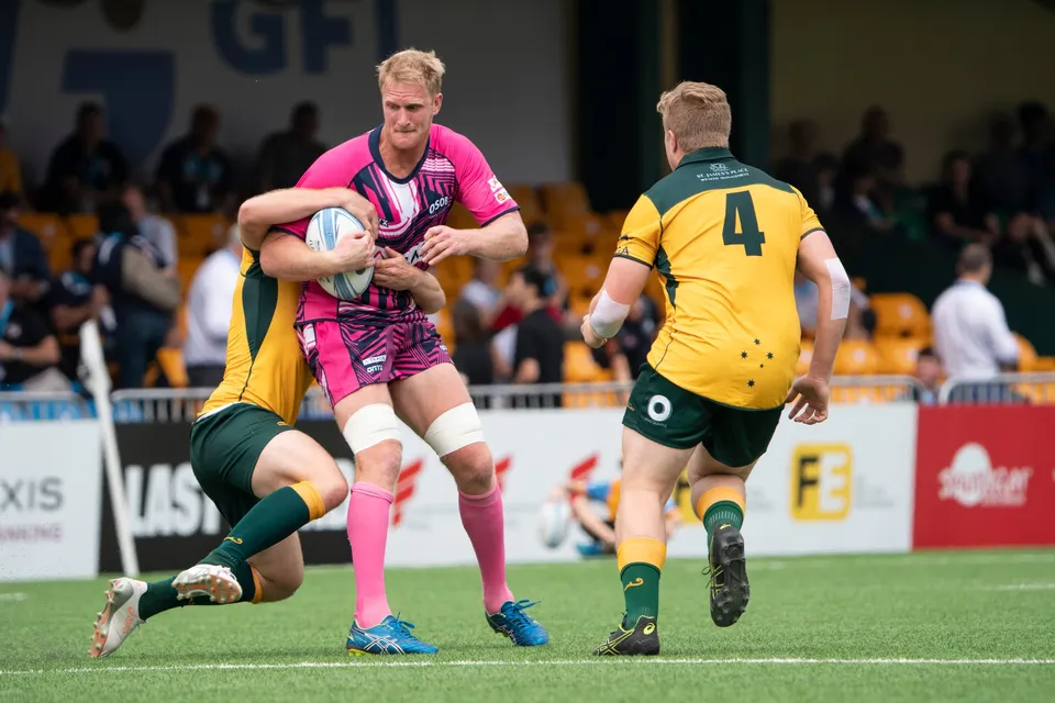 Blond OSOB ball carrier in pink is gripped round the legs by a Wallabies defender as number 4 closes in