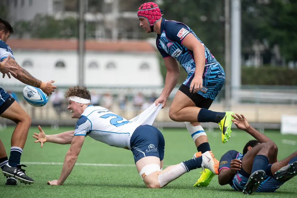 Irish Vikings player in white dives and flicks the ball away while an OSOB player in a red scrum cap looks on