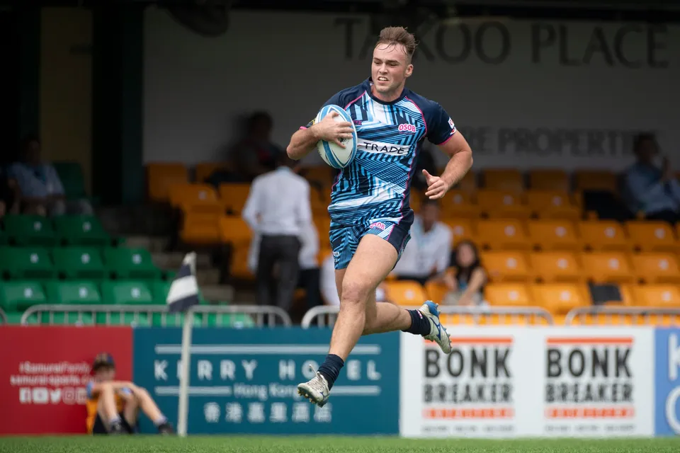 OSOB winger sprints along the touchline with the ball in both hands, advertising boards and stand behind