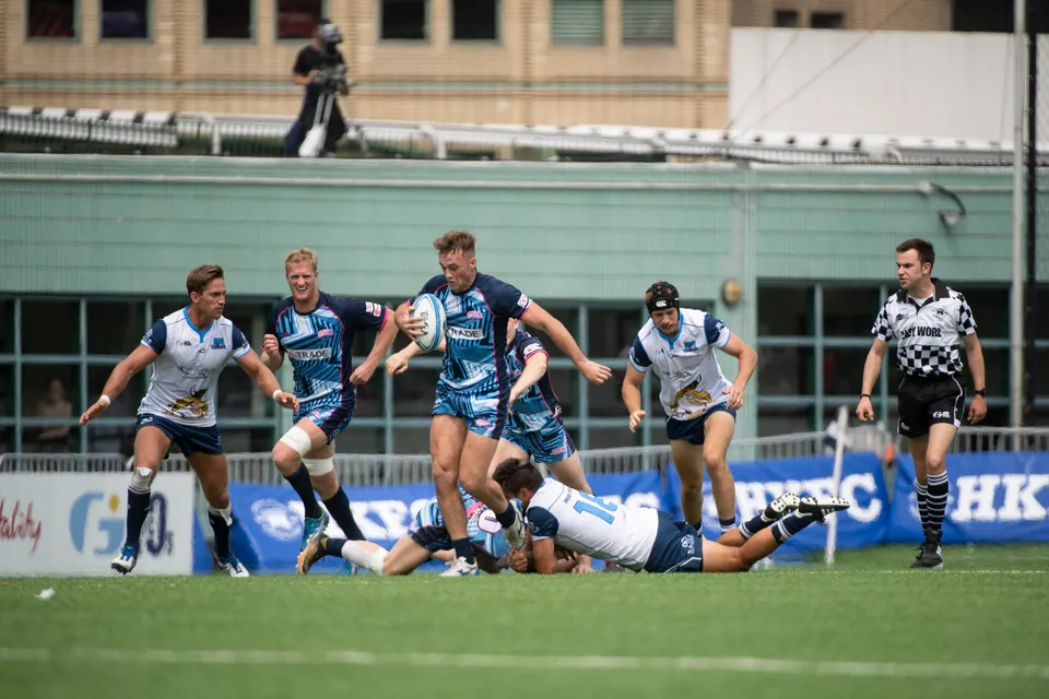 OSOB ball carrier runs at the Irish Vikings defence as a white-shirted player lies on the grass and the referee watches