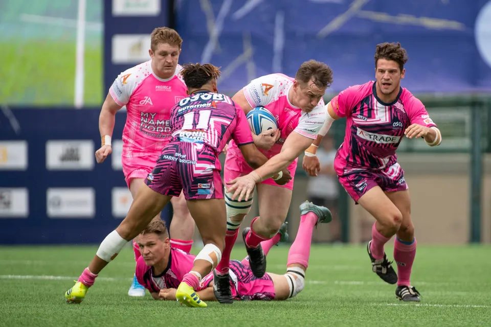 OSOB number 11 carries the ball into contact with pink-shirted Waterboys defenders while a team-mate lies on the grass