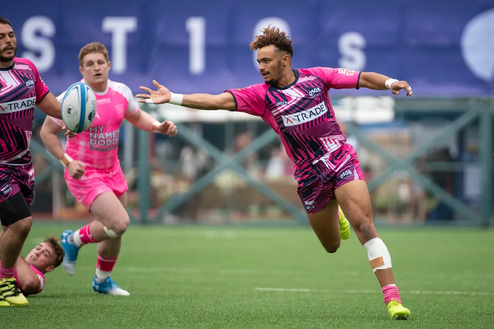 OSOB player in a patterned shirt reaches out an arm as a pink-shirted Waterboys player holds the ball, banner behind