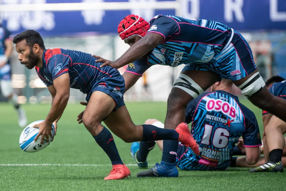 Navy-kit Scottish Exiles scrum half spins the ball out from a ruck while an OSOB number 16 lies on the ground