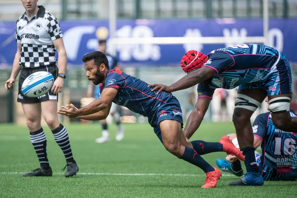 Scottish Exiles scrum half in navy dives into a pass from the ruck as a referee in black and white looks on