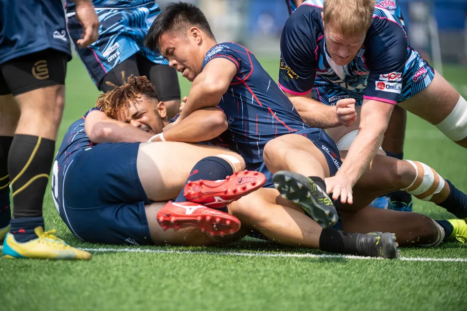 Players in navy kit pile onto the grass in a close tackle on the touchline during the 2019 Scottish Exiles match
