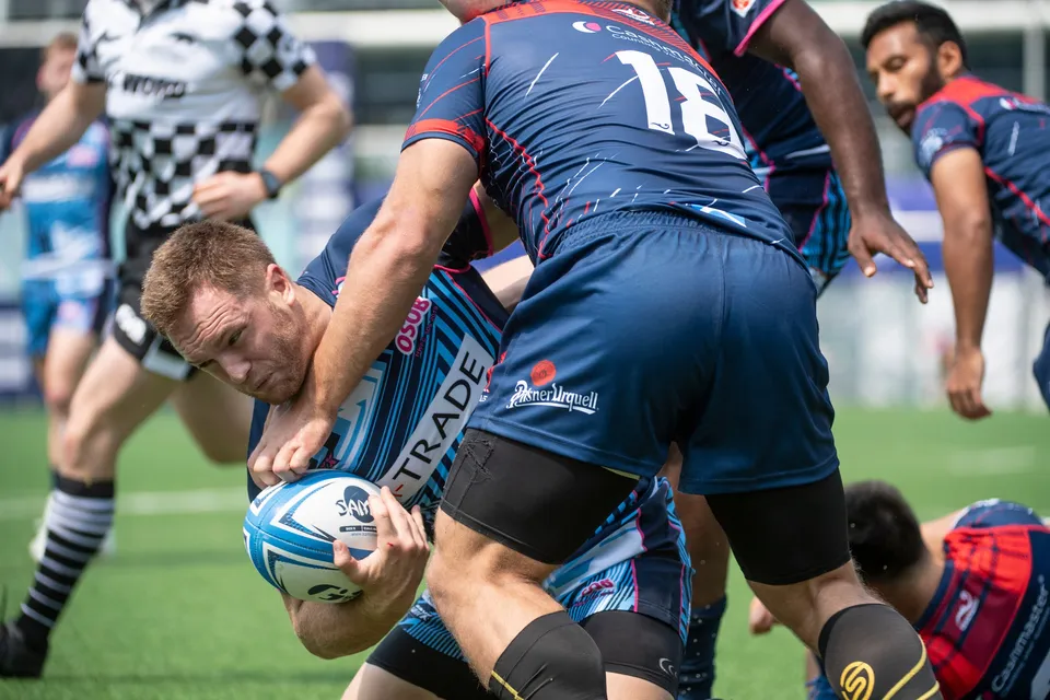 Ball carrier in light blue stripes is held by a navy defender wearing 18 as a referee in check watches, 2019