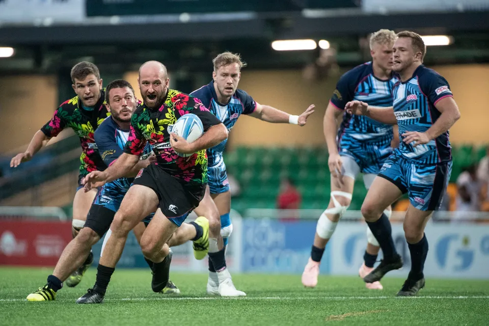 Ball carrier in a floral shirt runs at three blue-kit opponents with a team-mate on his shoulder, 2019 YCAC