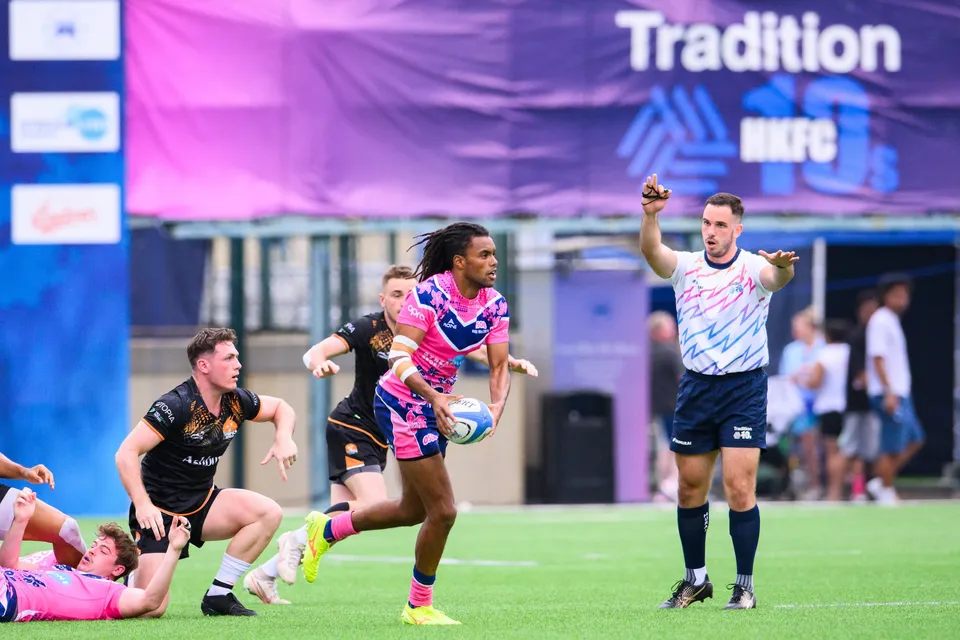 OSOB runner in pink and blue passes the ball as a referee signals and Ashbury Tropics players follow in 2024