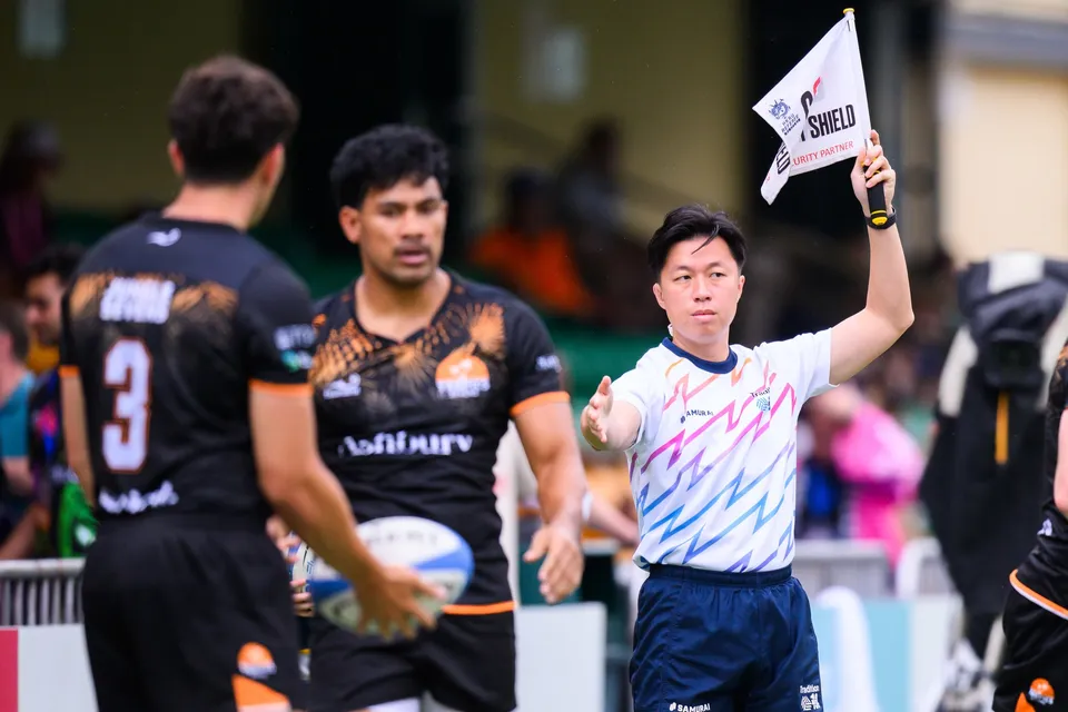 Ashbury Tropics player in black holds the ball in front of a flag-raising touch judge during OSOB match