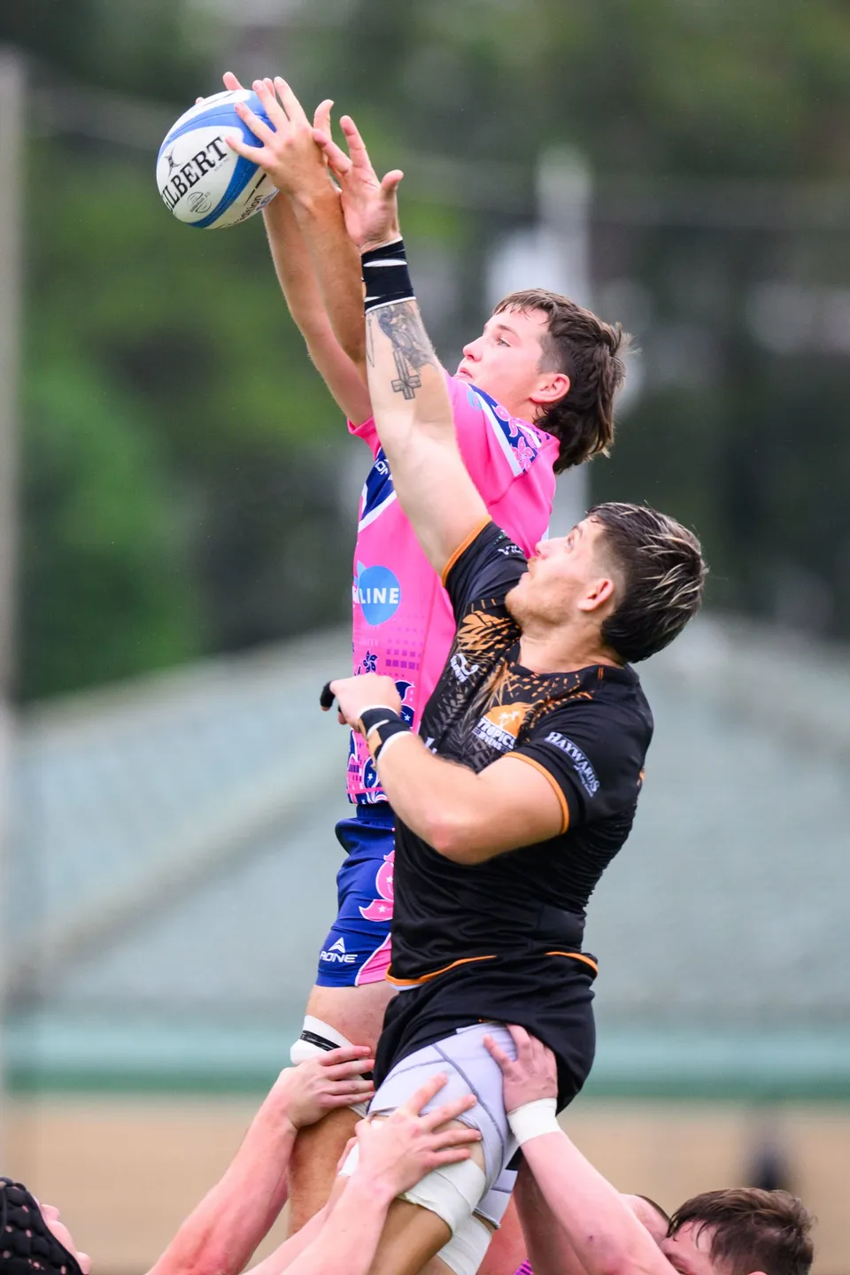 OSOB jumper in pink stretches high to catch the ball in a line-out against an Ashbury Tropics jumper in black