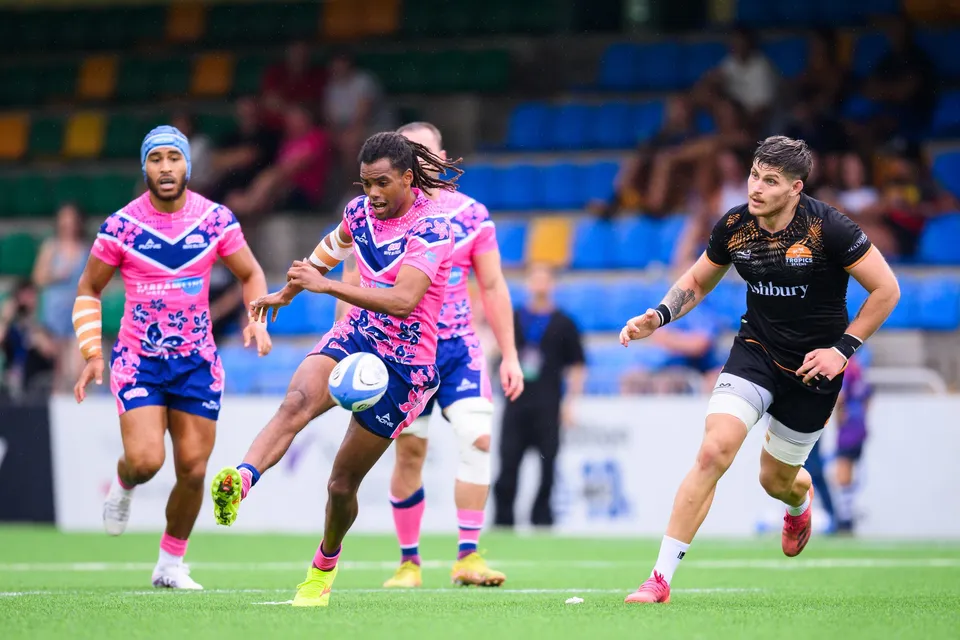 OSOB player with long hair moves the ball upfield, a teammate in a blue headguard and an Ashbury Tropics player behind