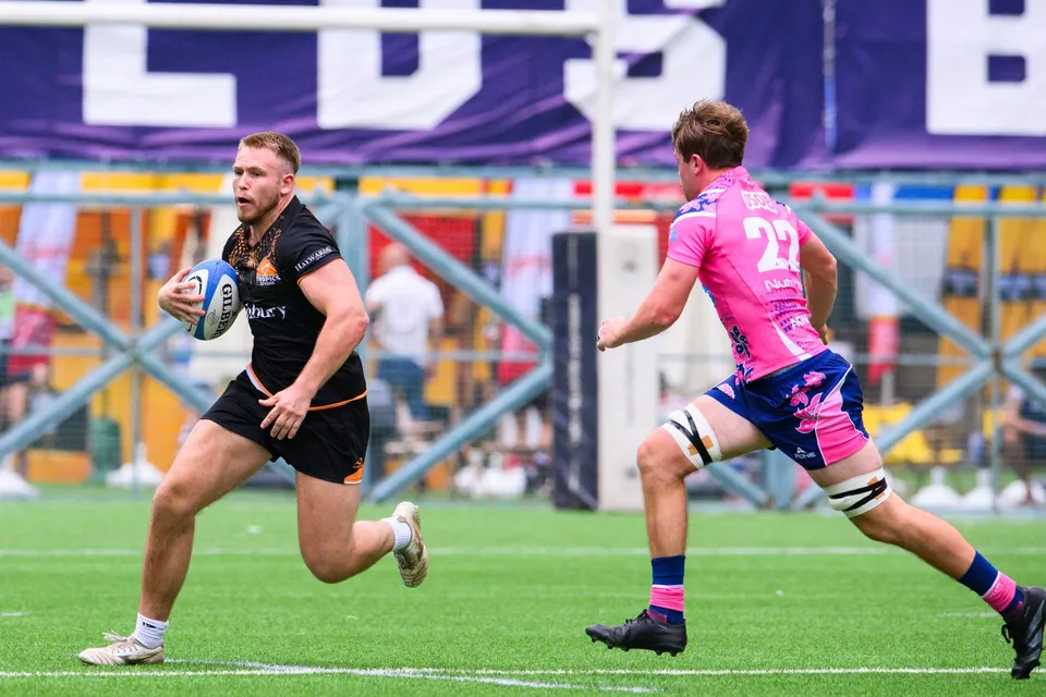 Ashbury Tropics player in black runs with the ball while OSOB number 22 closes in from the right