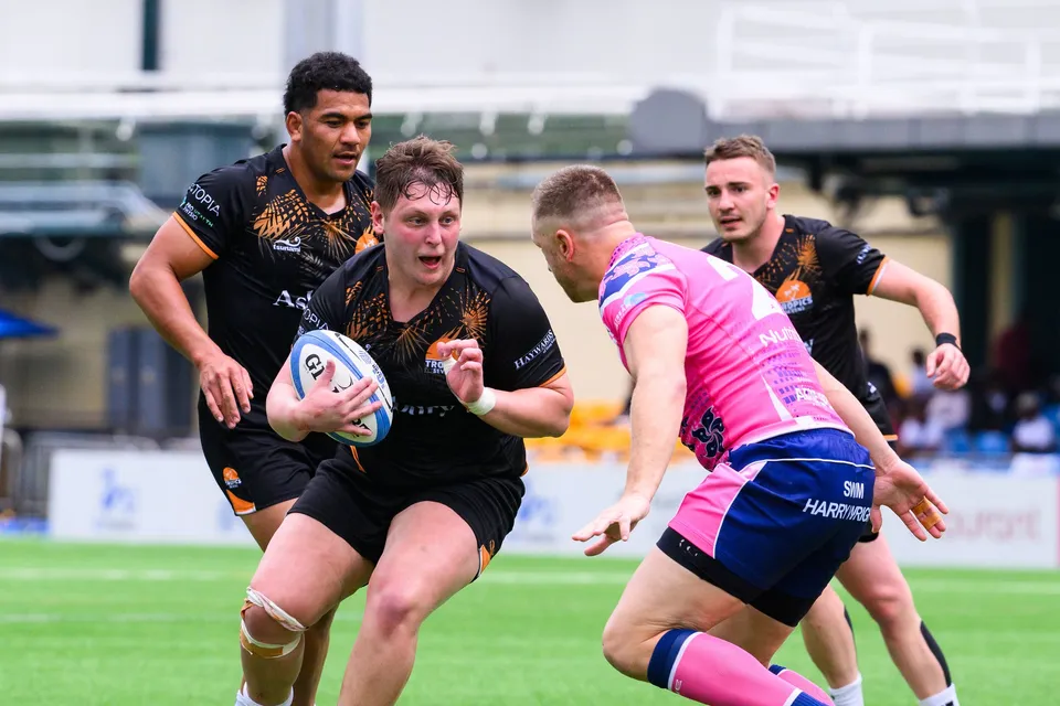 Ashbury Tropics forward carries the ball at an approaching OSOB player, a black-shirted teammate in support