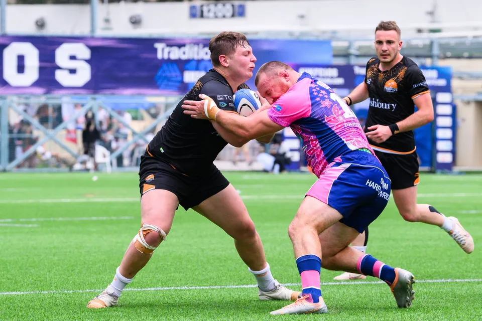 OSOB defender in pink meets an Ashbury Tropics ball carrier head-on in a tackle, with a Tradition HKFC 10s banner behind