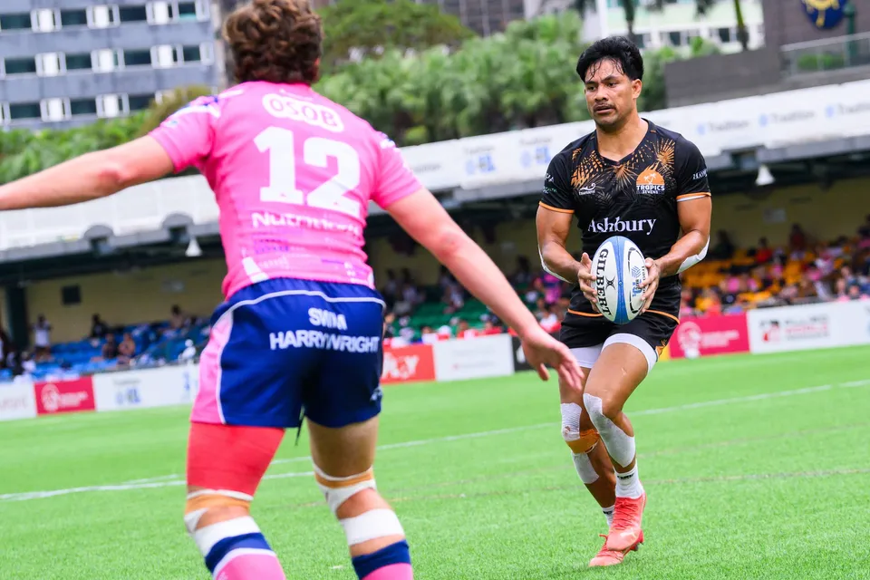 Ashbury Tropics player holds the ball facing OSOB number 12, who has his back to the camera, near the advertising boards