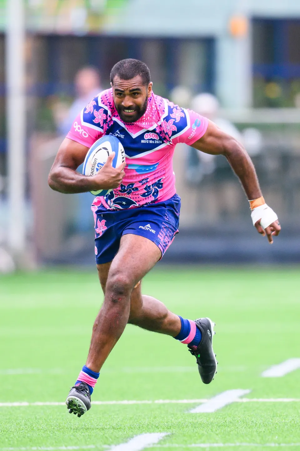 Smiling OSOB runner in pink and blue strides across the artificial turf with the ball tucked under one arm