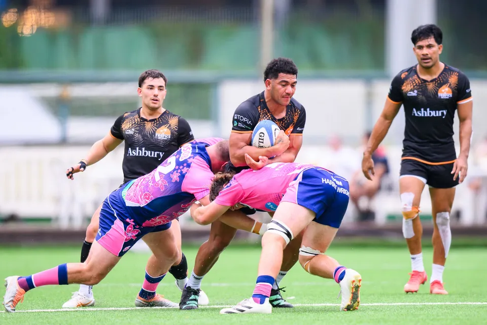 Two OSOB players tackle an Ashbury Tropics ball carrier low while two black-shirted teammates look on