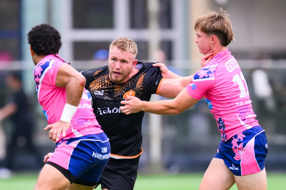Ashbury Tropics player in black is gripped by two OSOB defenders, one on each side, in a close-up of contact