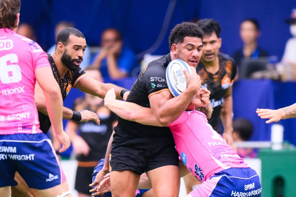 Ashbury Tropics ball carrier takes contact from OSOB defenders, a bearded black-shirted teammate arriving in support