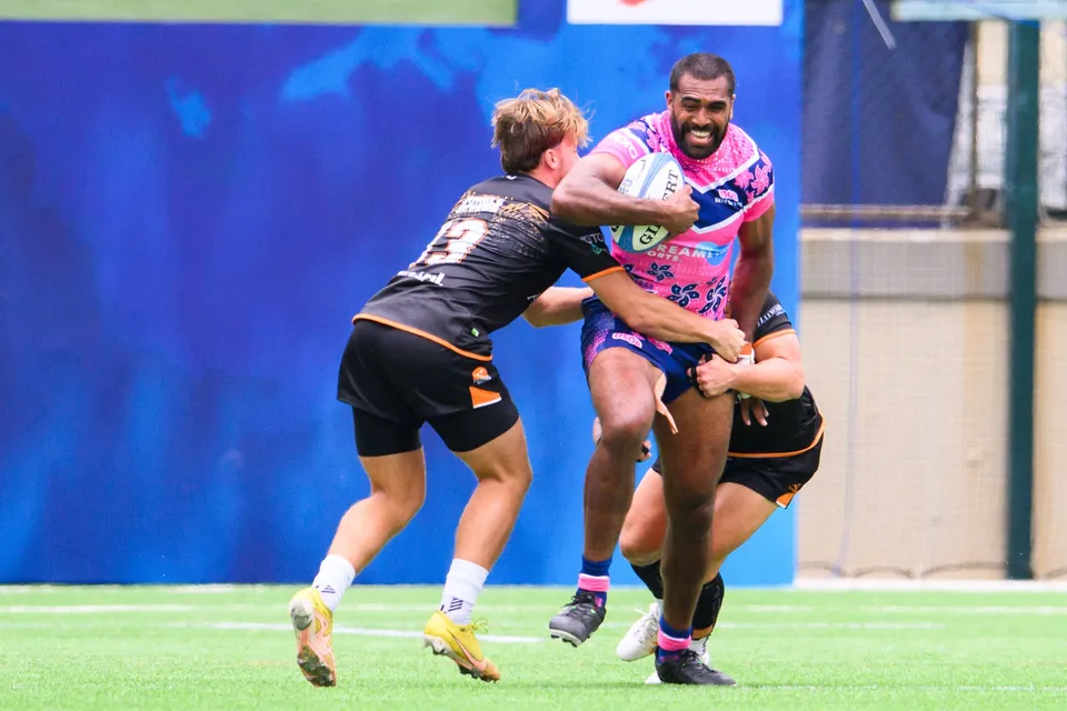 Smiling OSOB ball carrier powers through a tackle by Ashbury Tropics number 13, in front of a blue backdrop