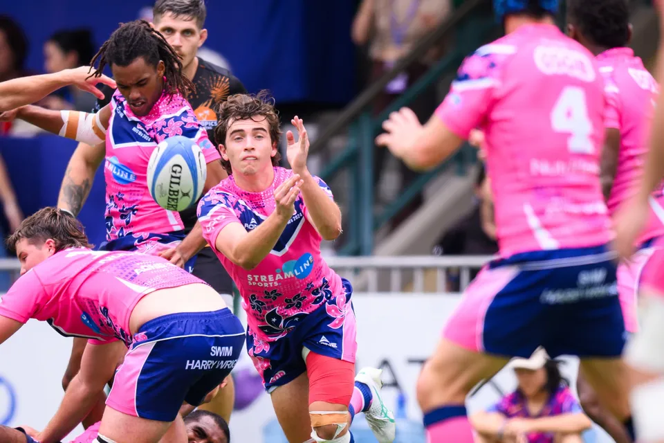 OSOB player with raised hands stands beside a long-haired teammate holding the ball, number 4 blurred in front