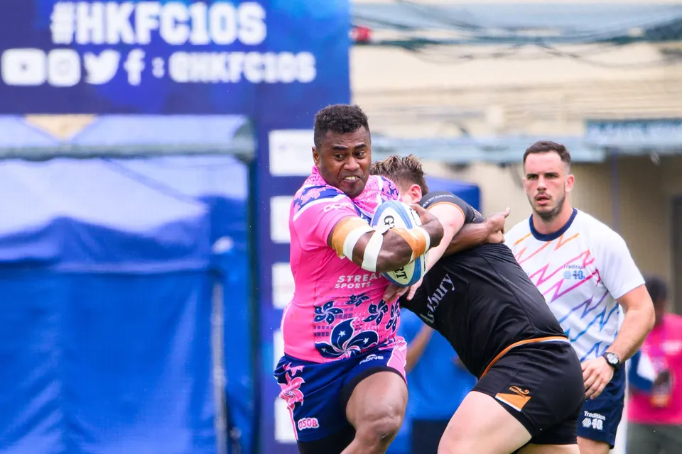 Close-up of an OSOB ball carrier held by an Ashbury Tropics tackler with a referee watching from the right