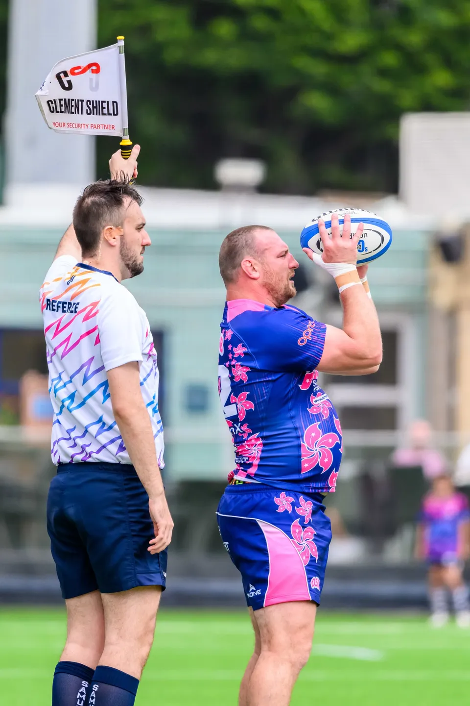 Referee with a flag stands beside an OSOB forward holding the ball overhead, apparently ready to throw in