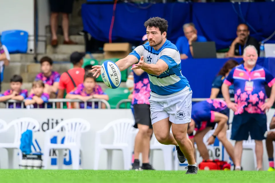 HKFC Natixis runner reaches out to pass the ball as young spectators and OSOB team-mates watch from behind