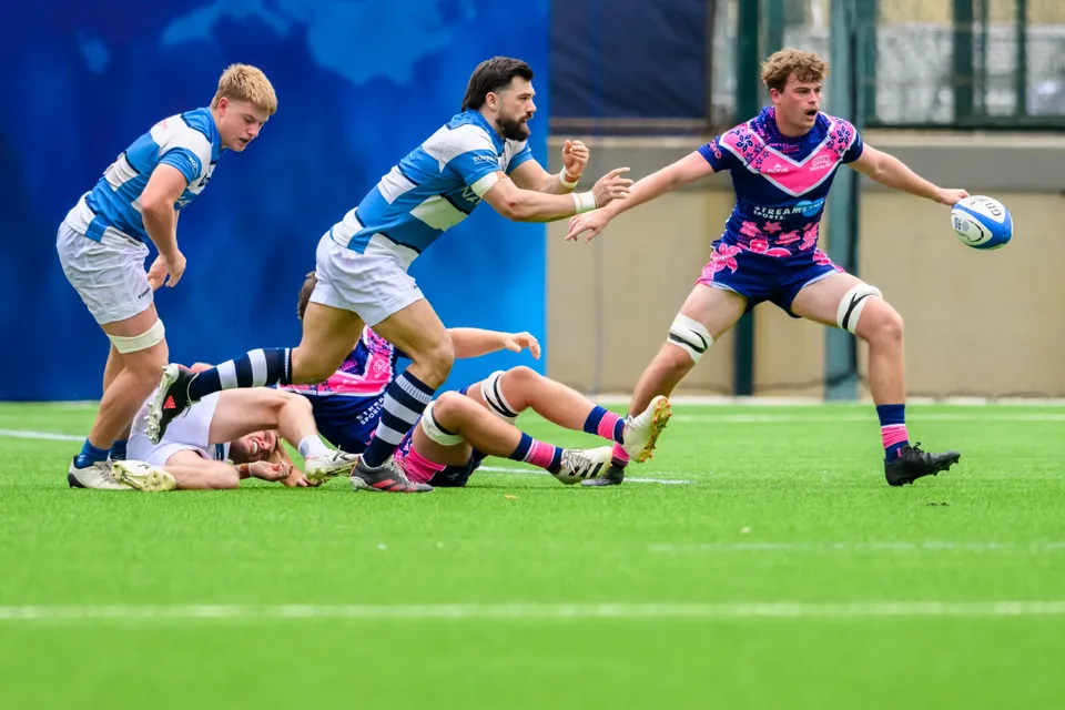 OSOB player reaches for a loose ball as light blue HKFC Natixis runners pass and others lie on the grass