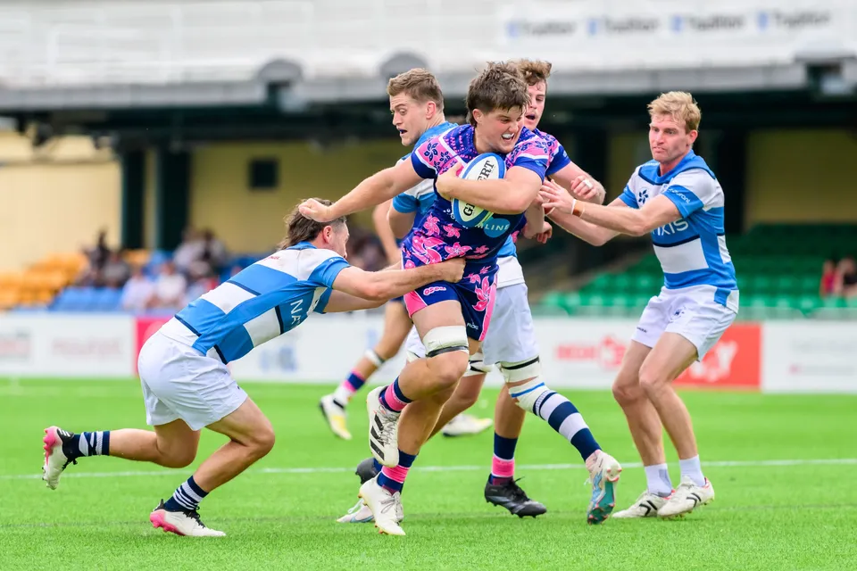 OSOB ball carrier is held up by two blue and white HKFC Natixis defenders, with a third defender close by