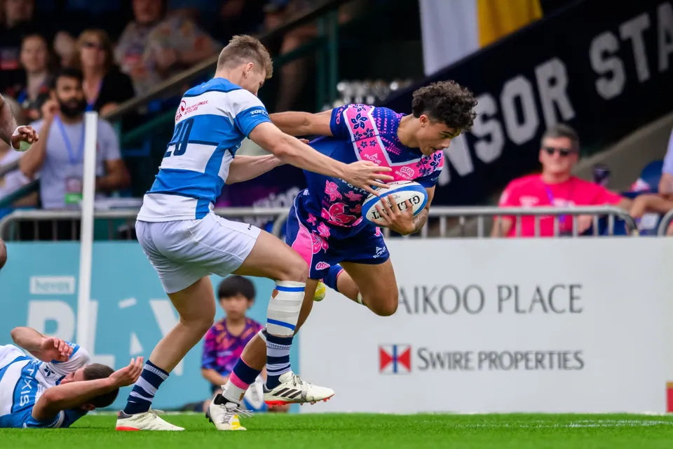 OSOB player leaps sideways with the ball as an HKFC Natixis defender in number 20 reaches to tackle him