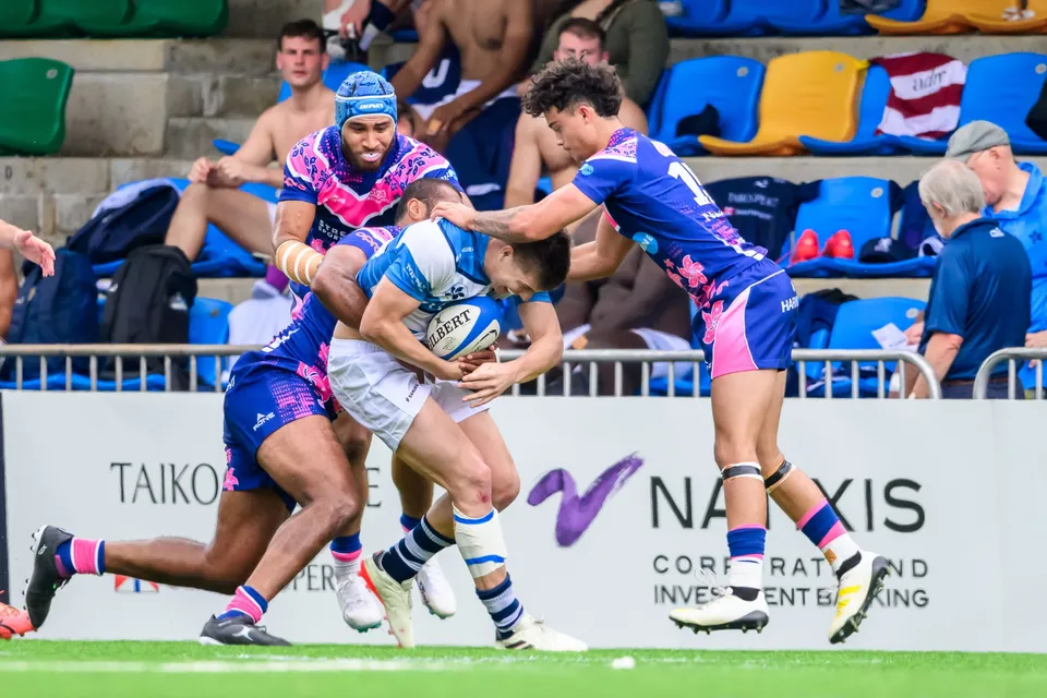 OSOB ball carrier is tackled by an HKFC Natixis defender in front of a Natixis board as a teammate runs in