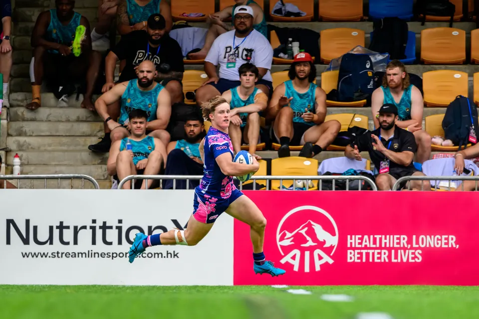 OSOB winger sprints along the touchline with the ball past an AIA advertising board and spectators in the stand