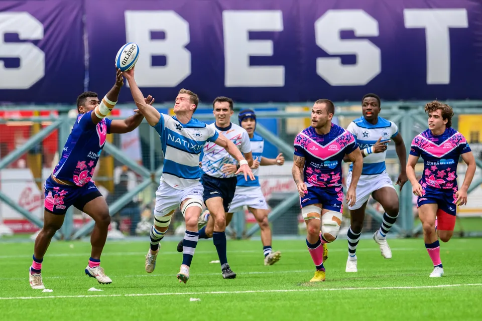 OSOB player jumps to claim a high ball as HKFC Natixis and OSOB players watch beneath a large purple banner