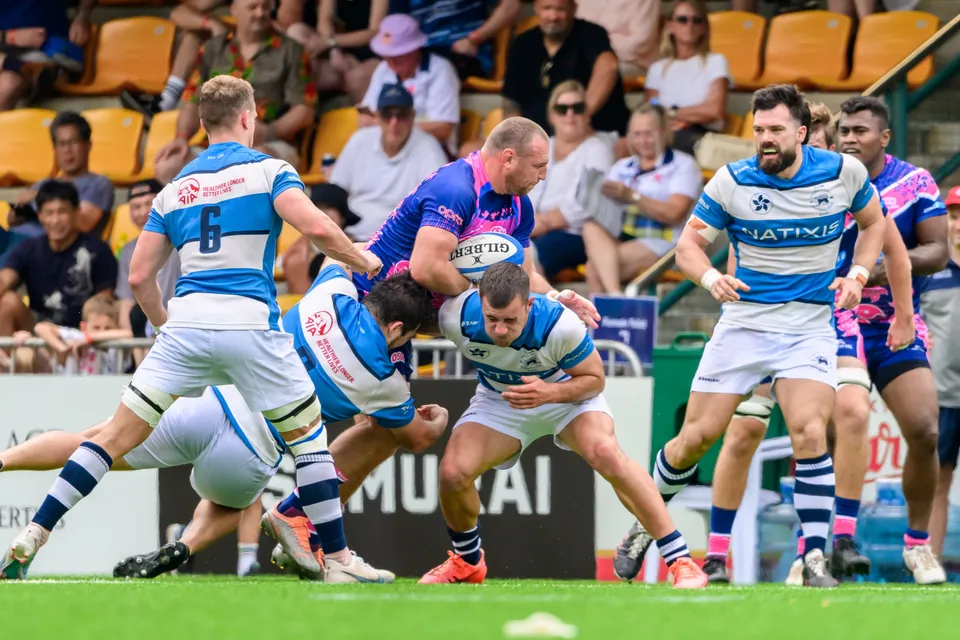 OSOB ball carrier is gripped at chest height by HKFC Natixis defenders, number 6 among them, with spectators behind