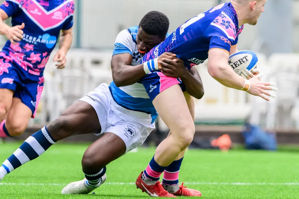 OSOB ball carrier is tackled around the waist by an HKFC Natixis defender as the ball swings out in his right hand