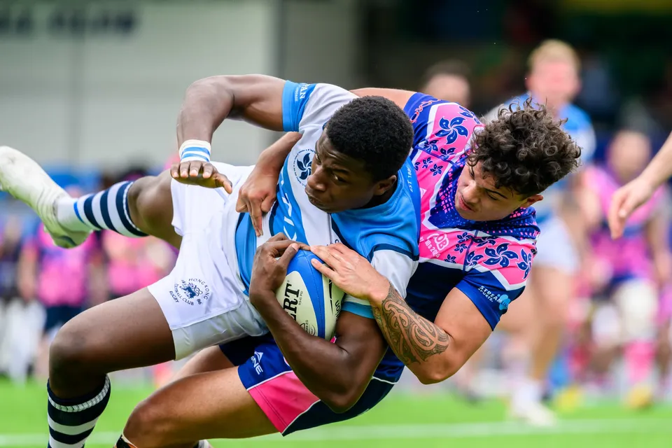 Tight shot of an HKFC Natixis player clutching the ball while an OSOB tackler pulls him down
