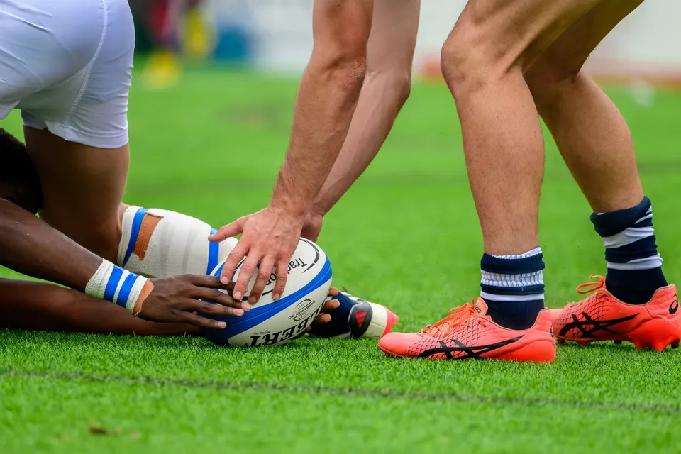 Close view of a ball on the grass at a breakdown, hands reaching for it beside orange boots and striped socks