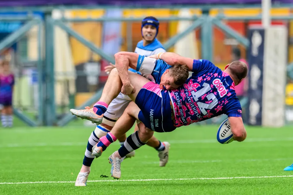 OSOB number 12 is tipped sideways in a tackle with the ball low and an HKFC Natixis player over him