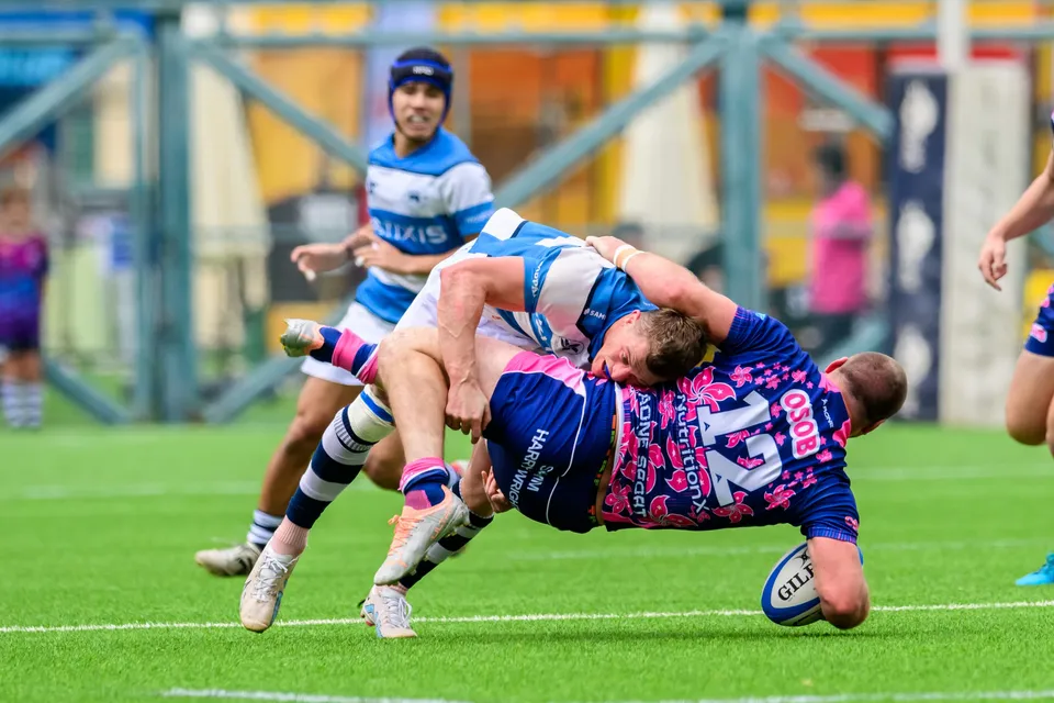 OSOB number 12 comes down flat on the grass in a tackle, the ball by the turf as HKFC Natixis players watch