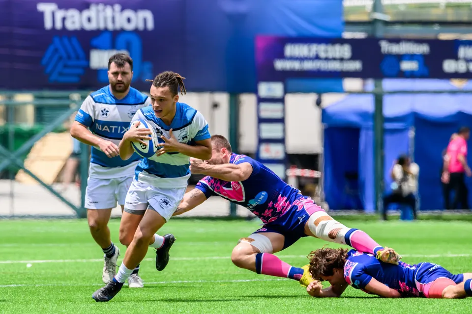HKFC Natixis runner breaks through as an OSOB defender grabs at his waist and a teammate lies on the turf