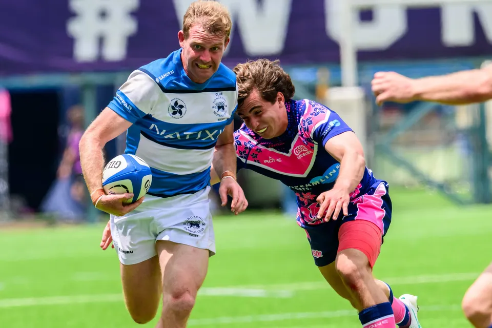 Close-up of a smiling HKFC Natixis player carrying the ball with an OSOB defender running right alongside him