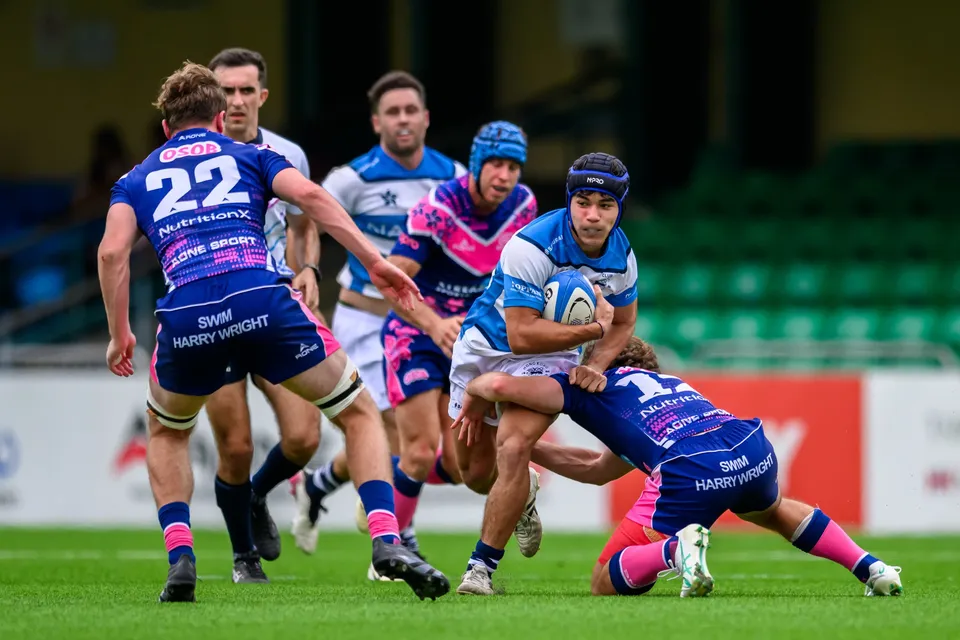 HKFC Natixis runner in a blue headband holds the ball as an OSOB player lunges low, with number 22 behind